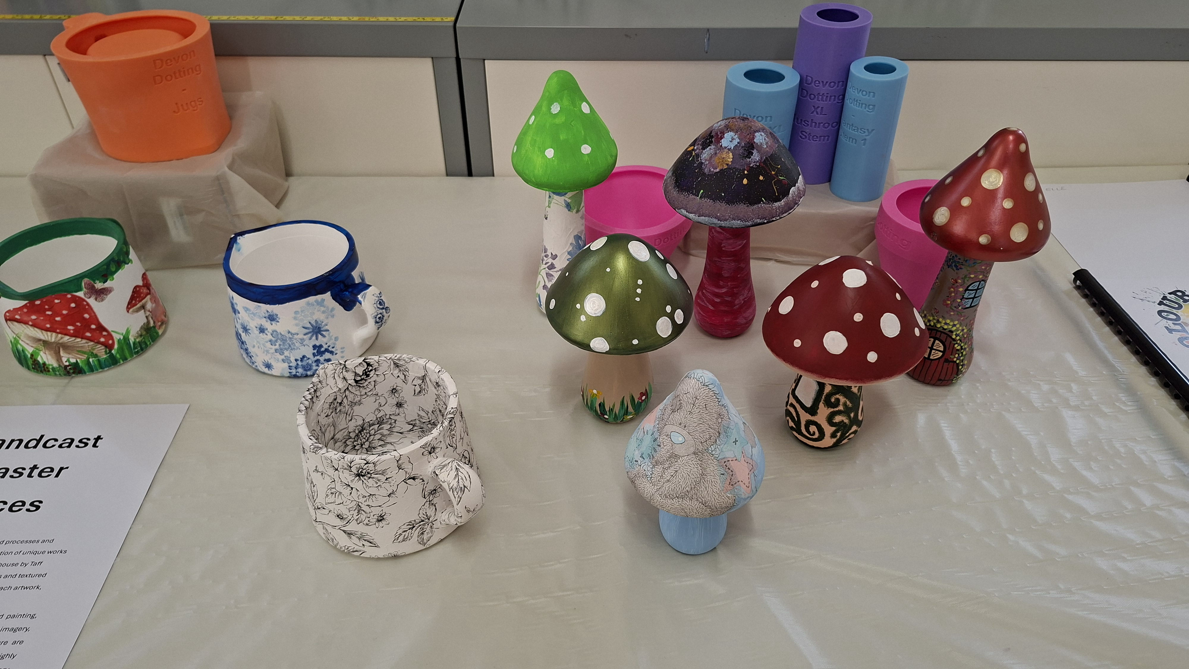 Colourful handcrafted mushroom pieces displayed on a table with painted designs. Bright tones and playful patterns create a whimsical atmosphere.