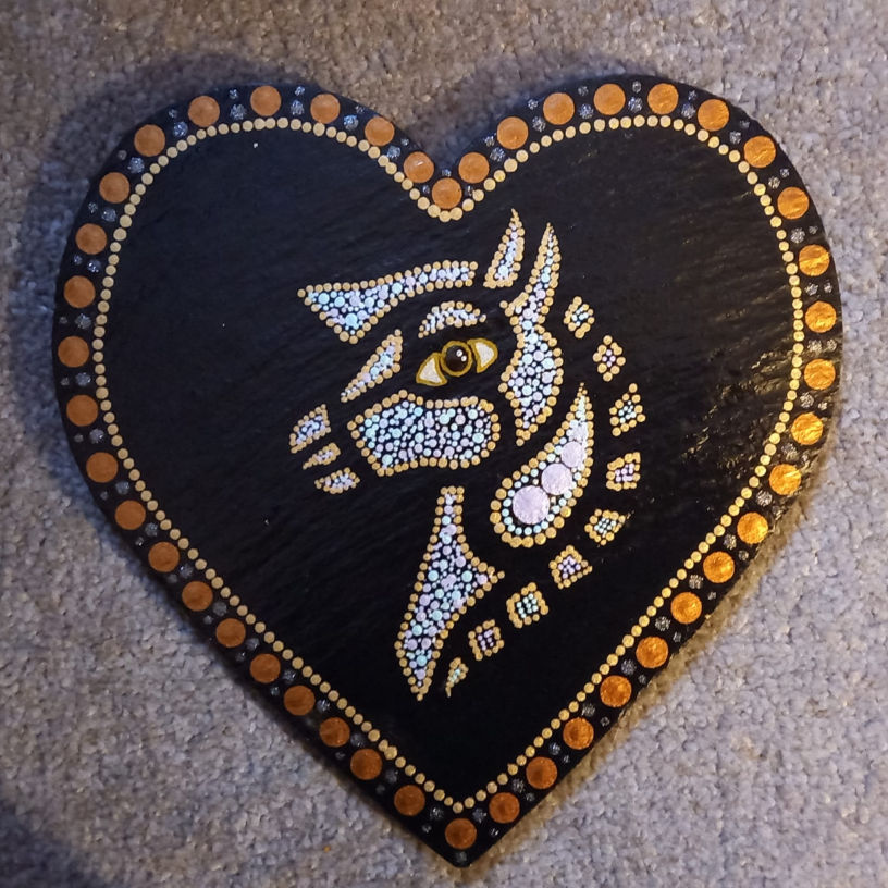 Heart-shaped artwork on slate with a geometric horse design in white dots and gold accents. Border has alternating gold and orange dots.