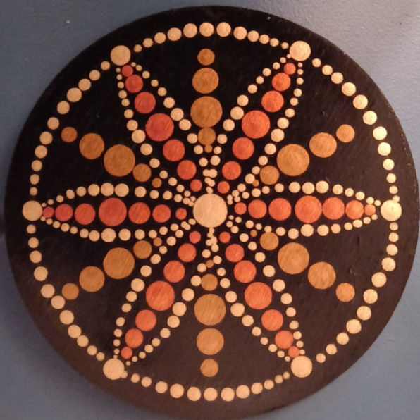 A circular mandala with a black background, featuring intricate dot patterns in white, orange, and brown, forming symmetric petal-like designs.