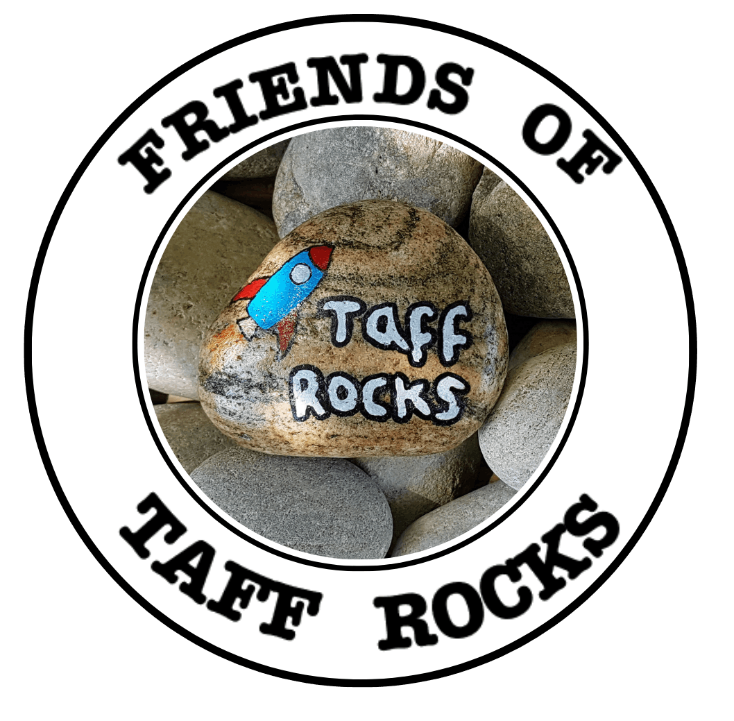 A round logo with "Friends of Taff Rocks" in bold text. At the center, a painted rock features a blue-red rocket and the words "Taff Rocks" on a bed of stones.