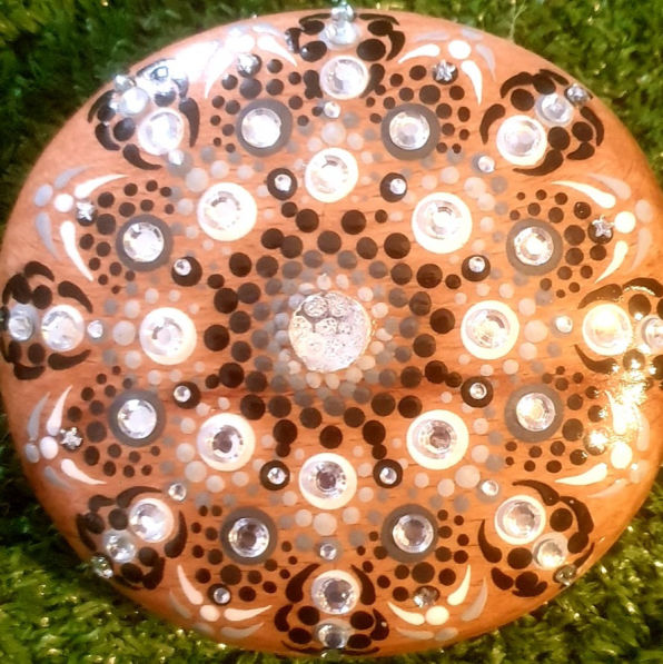 Mandala rock art featuring intricate black, white, and silver dot patterns with sparkling gemstones on a green grass background, evoking harmony.