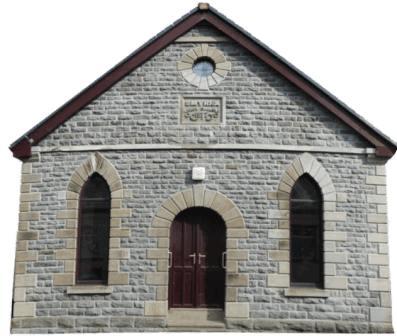 The Smyrna building. A small stone chapel with a classic gabled roof and arched windows. The entrance features a wooden door. The building evokes a serene, historical ambiance.